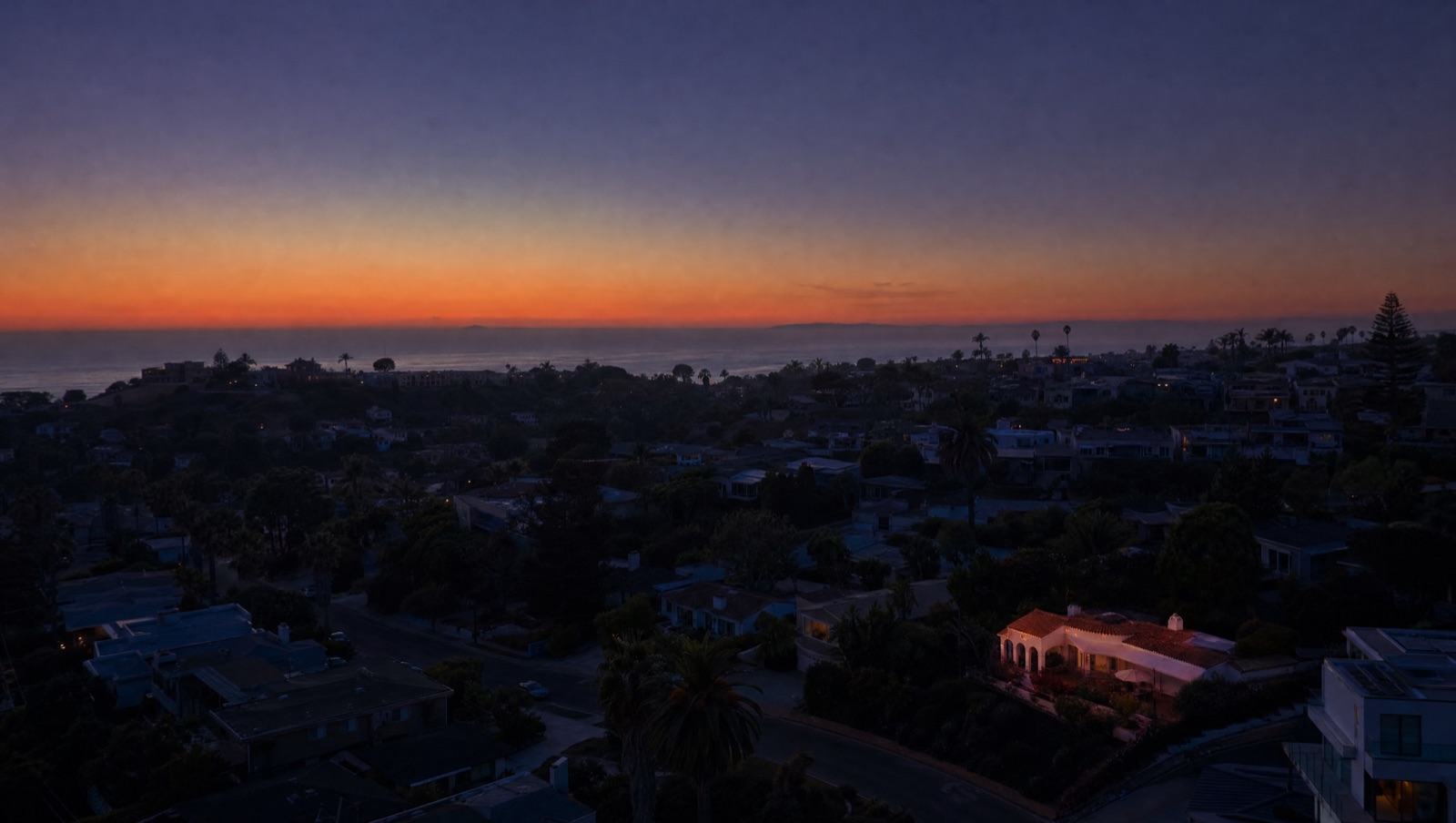 Aerial view of a coastal Southern California neighborhood at first light, a few rooftops catching dawn