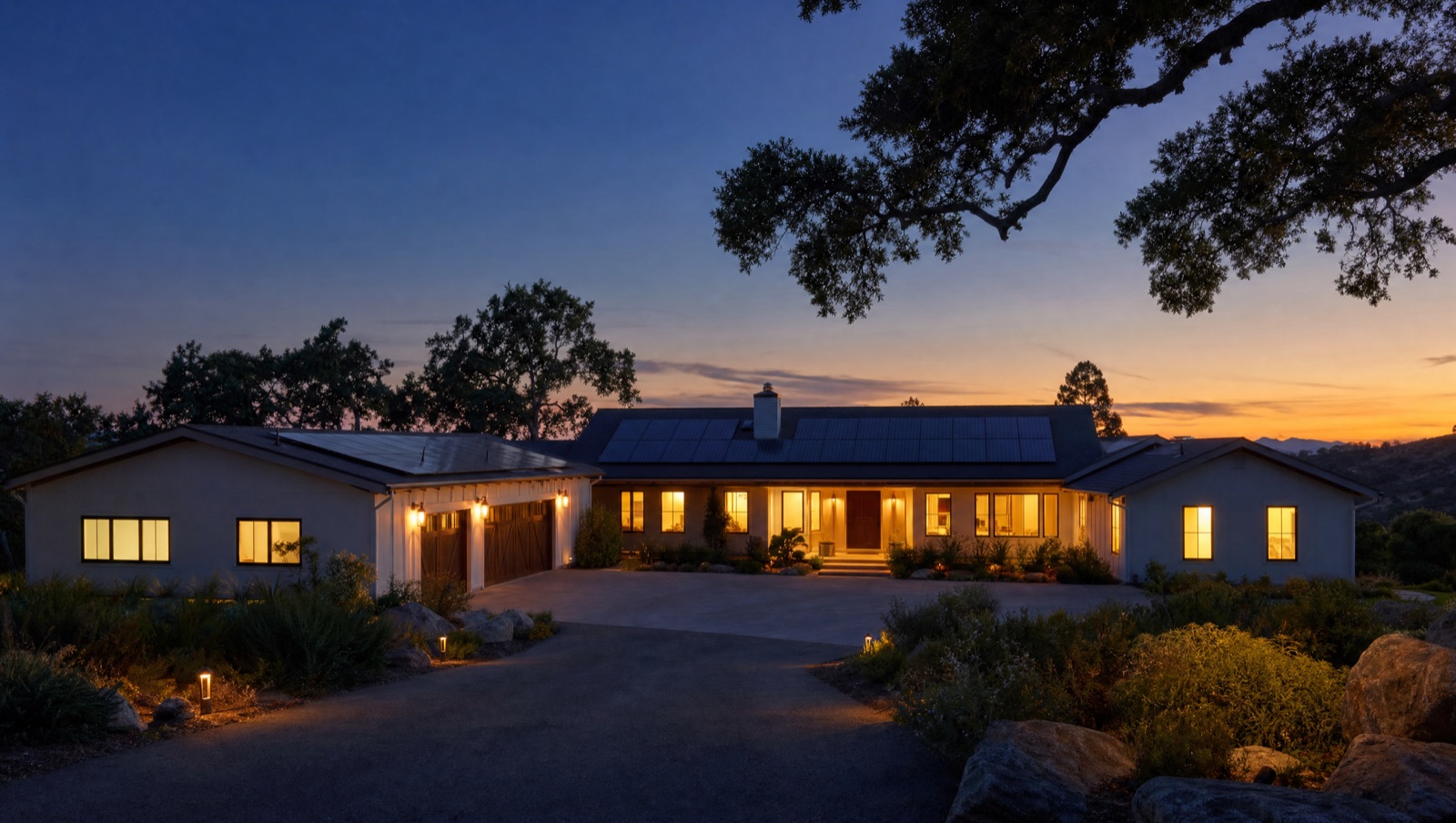 A California home at blue-hour evening, windows glowing warm, the day's sun banked